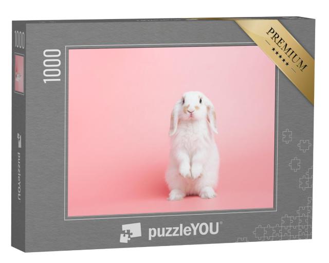 Puzzel 1000 stukjes „Een wit konijn met hangende oren poseert voor een roze achtergrond“