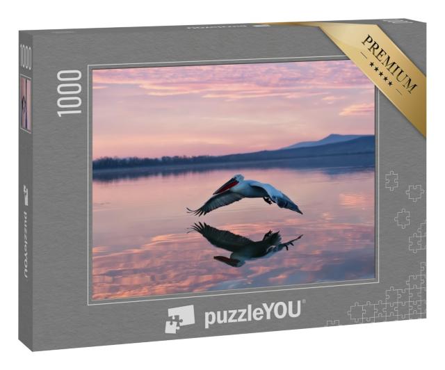 Puzzle 1000 Teile „Schweben über dem Wasser: Pelikan im Sonnenaufgang“